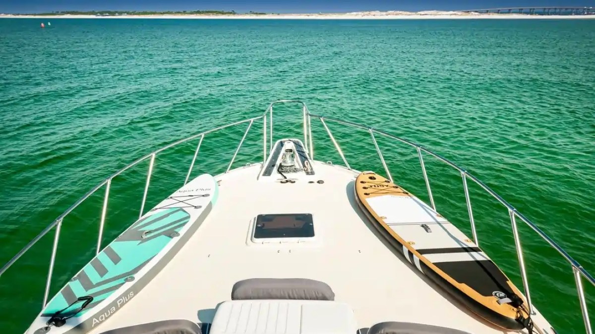 Boat deck with blue and brown paddleboards on green water, distant shore visible.