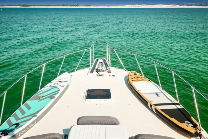 Boat deck with blue and brown paddleboards on green water, distant shore visible.