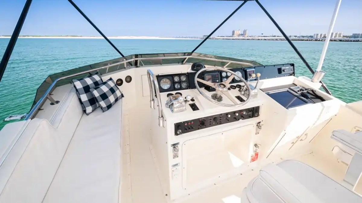 Boat cockpit with steering wheel, controls, checkered cushion, and ocean view.