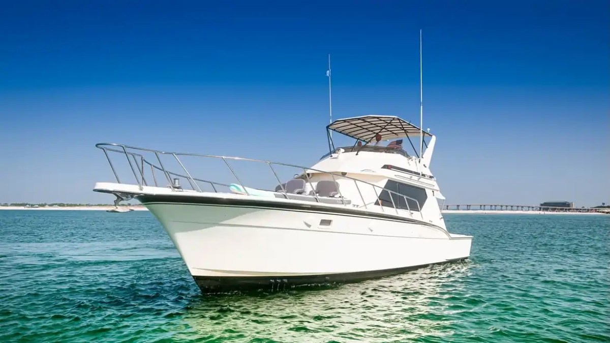 White yacht sailing on clear blue water under a clear blue sky.