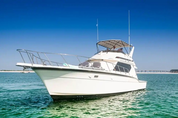 White yacht sailing on clear blue water under a clear blue sky.