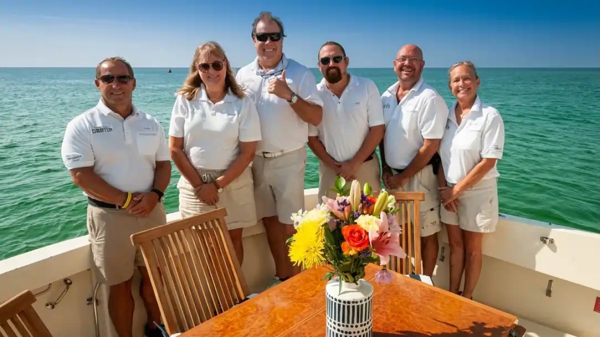 Group of six people in matching attire on a boat, with a floral centerpiece on a table.