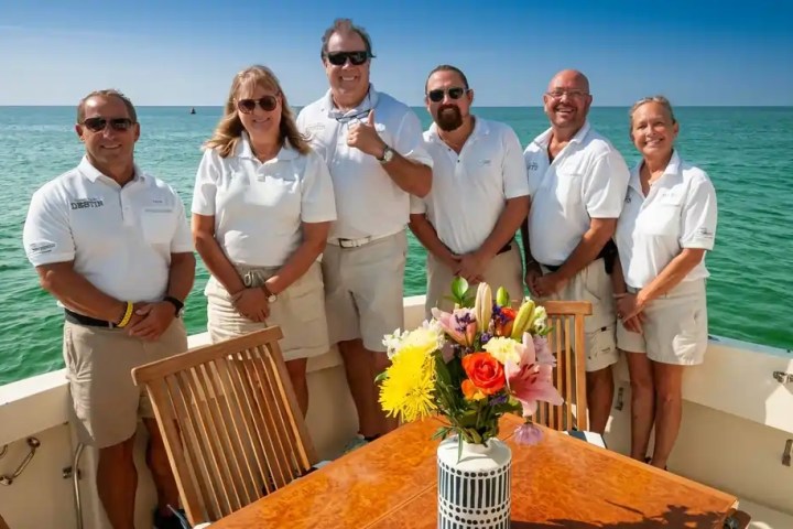 Group of six people in matching attire on a boat, with a floral centerpiece on a table.