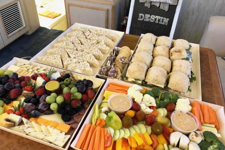 Assorted platters of fruits, vegetables, sandwiches, and rice treats with a welcome sign in background.