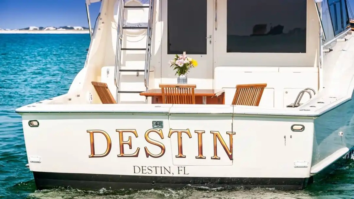 The back of a boat named 'Destin' with a table and chairs on deck, floating in blue water.