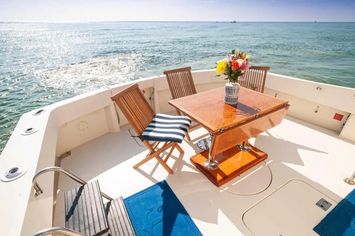 Boat deck with wooden chairs, table, and flower vase overlooking the sea.