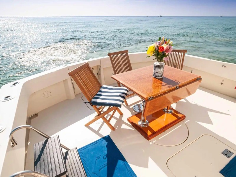 Boat deck with wooden chairs, table, and flower vase overlooking the sea.