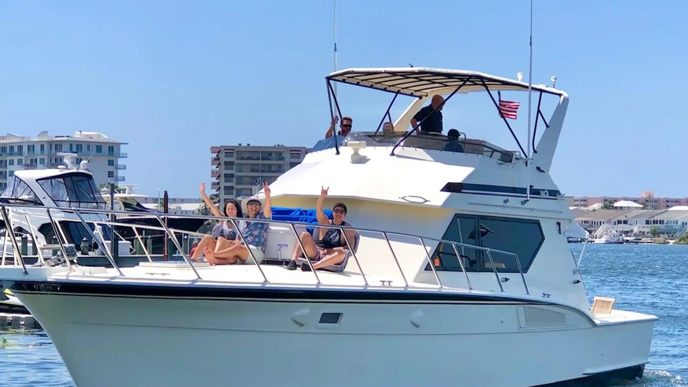 People relaxing on a yacht in a marina with buildings in the background.