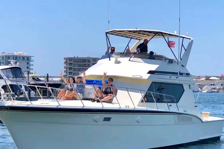 People relaxing on a yacht in a marina with buildings in the background.
