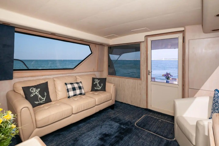 Yacht interior with beige sofa, anchor pillows, blue rug, and ocean view.