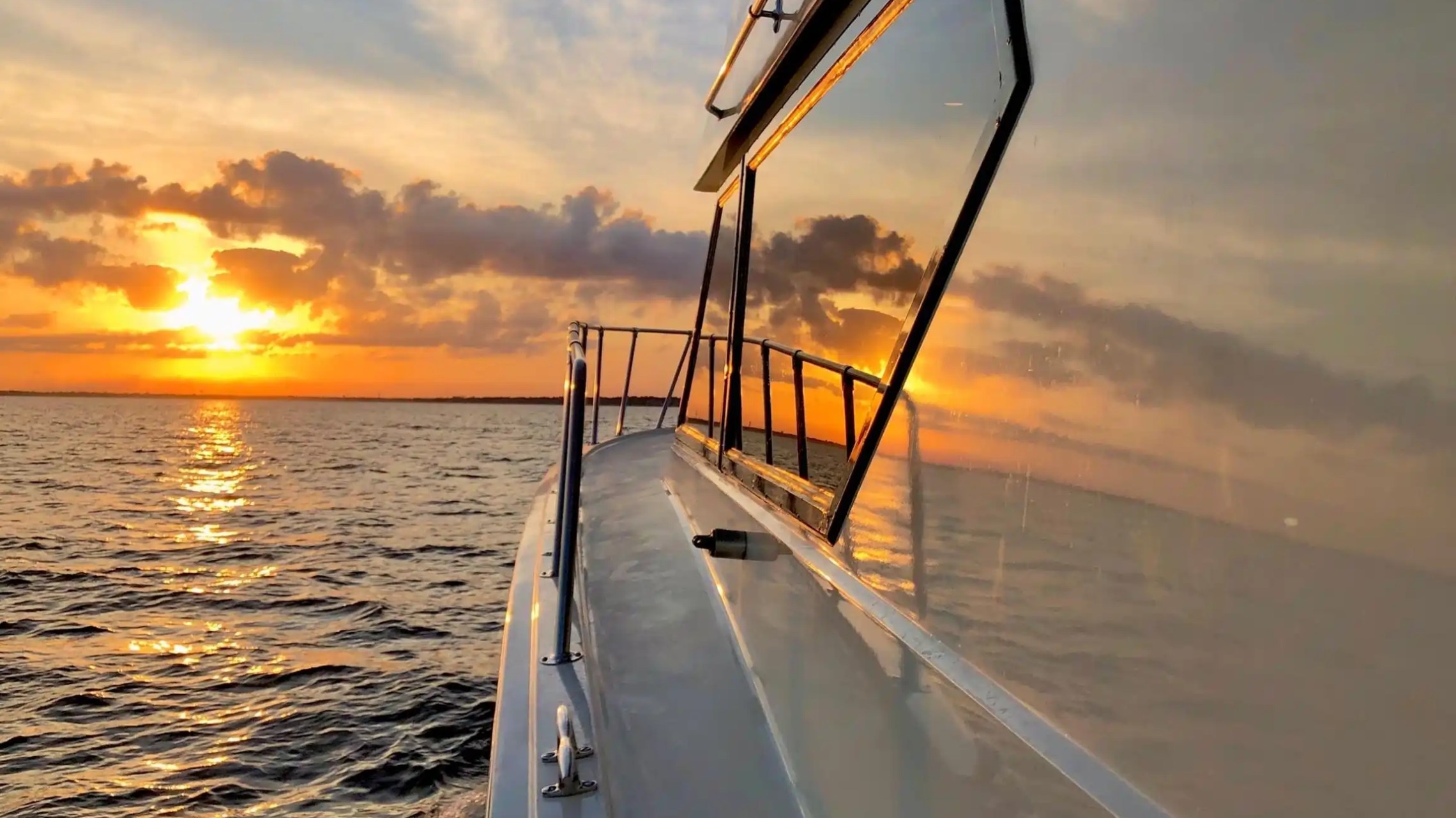 Boat on water with sunset and cloudy sky reflected on its window.