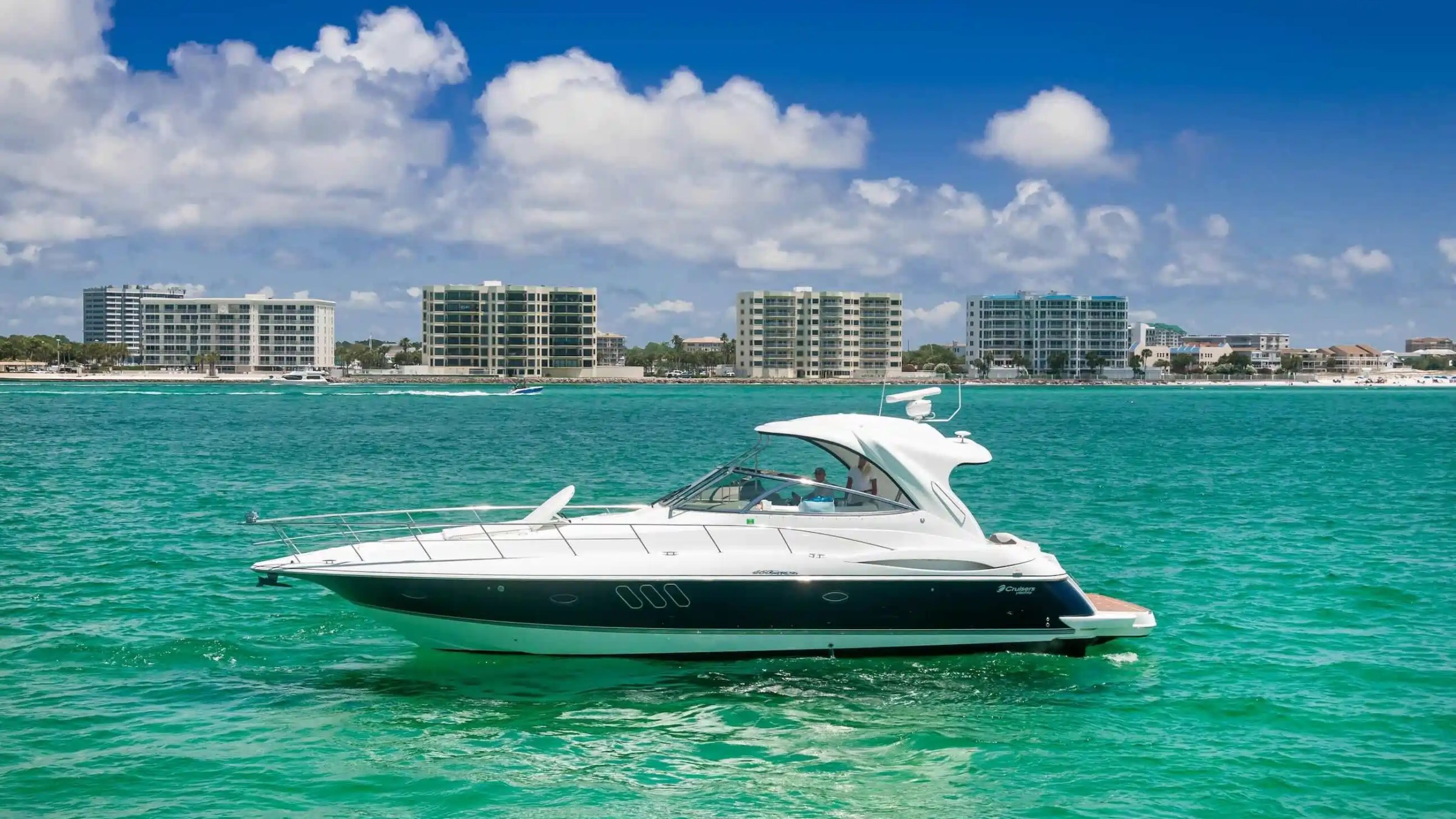 Luxury yacht on turquoise water with a city skyline in the background.