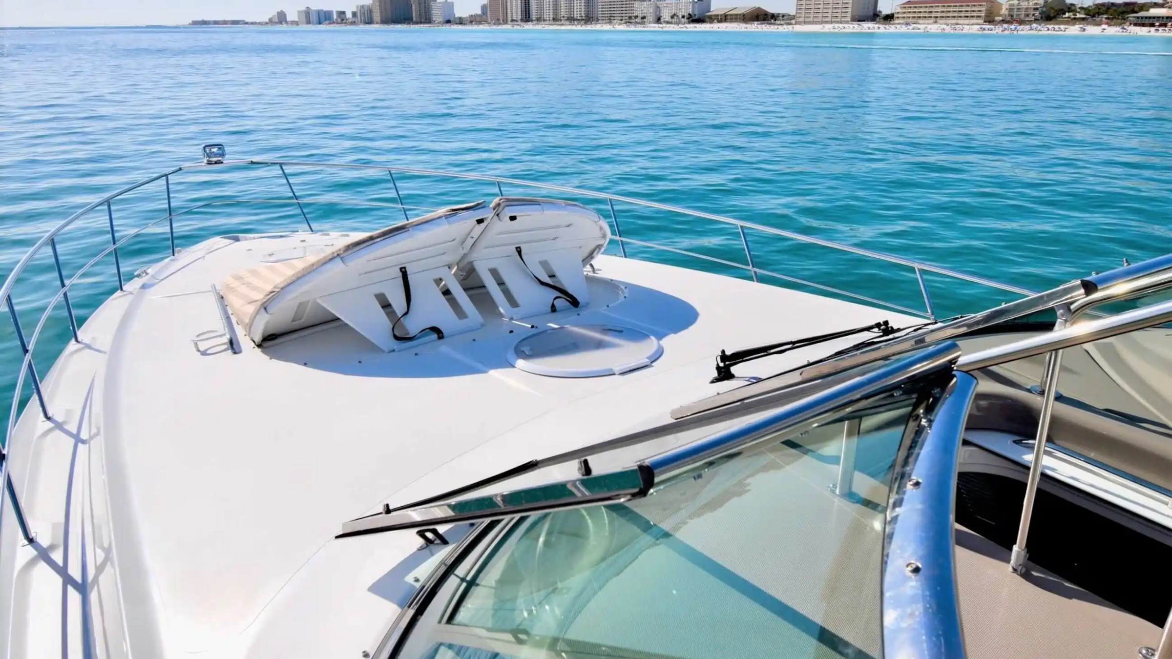 View from yacht deck over clear ocean towards distant city skyline.