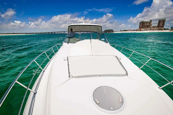 View from yacht deck toward beach with buildings and pier in the distance on a sunny day.