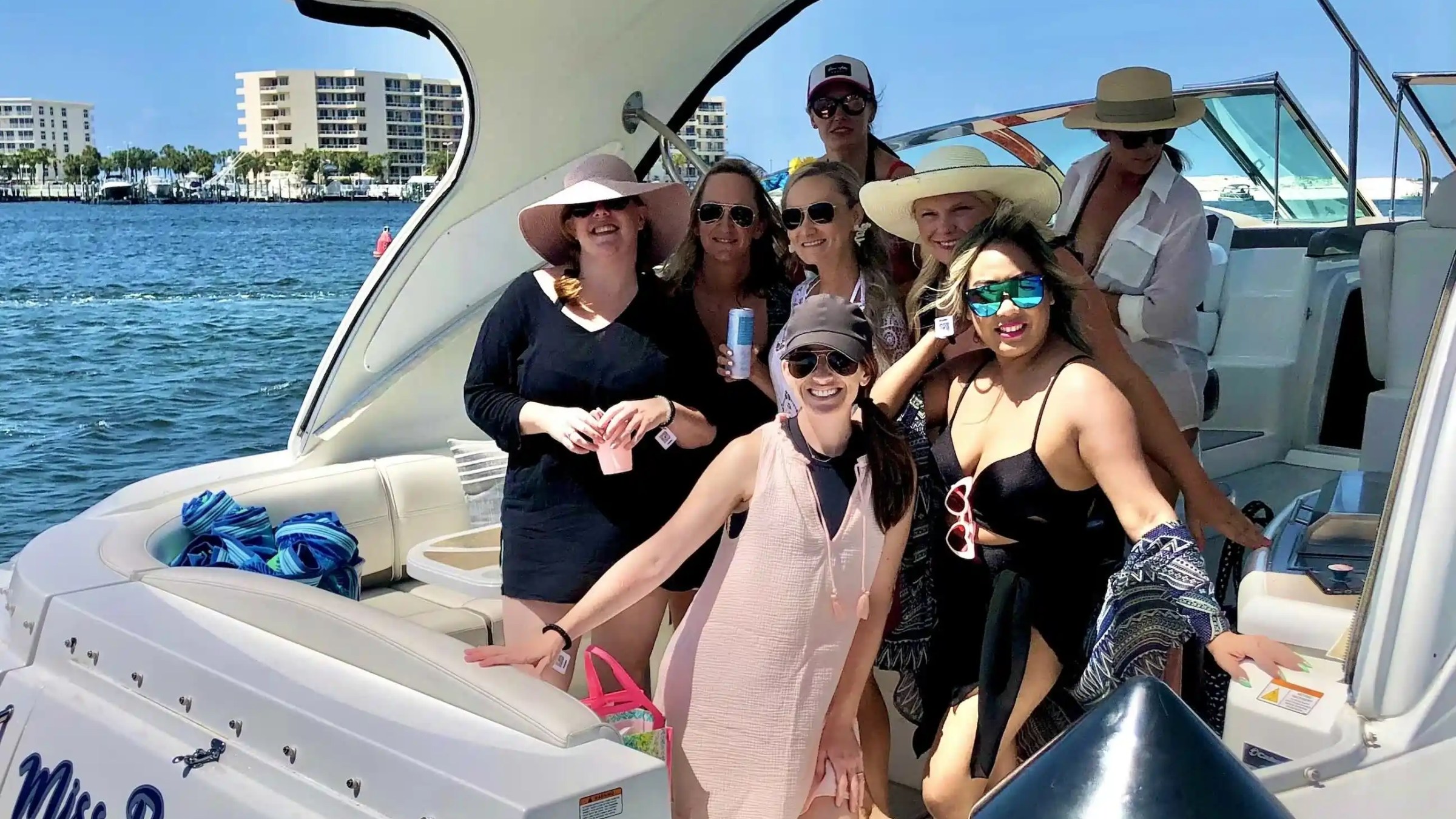 Group of people on a boat enjoying a sunny day, with some wearing hats and sunglasses.