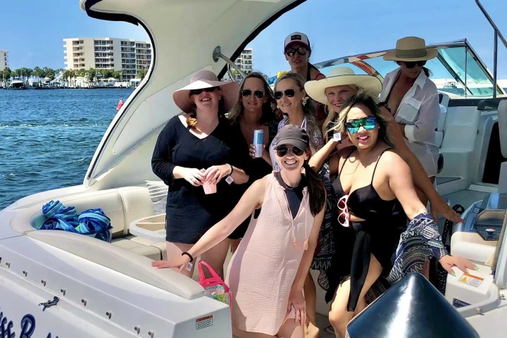 Group of people on a boat enjoying a sunny day, with some wearing hats and sunglasses.