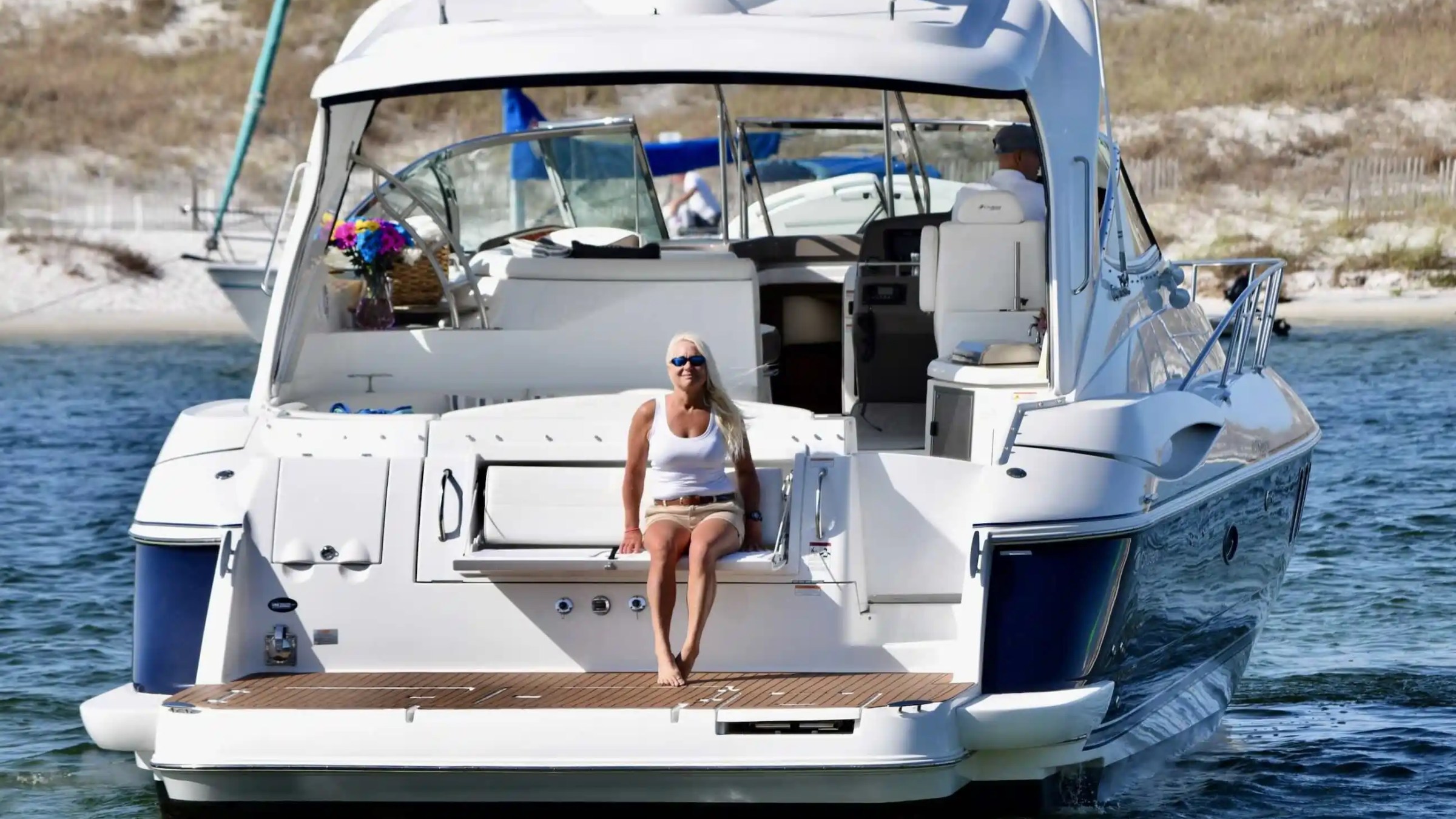 Woman sitting on the back of a white yacht in a sunny coastal area.