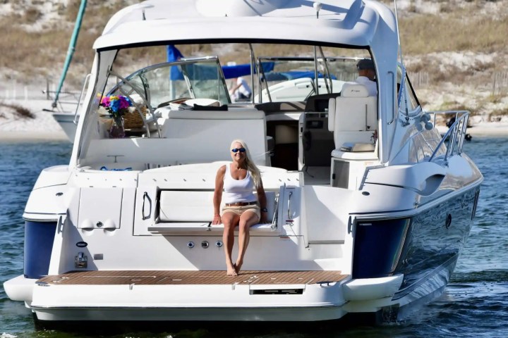 Woman sitting on the back of a white yacht in a sunny coastal area.