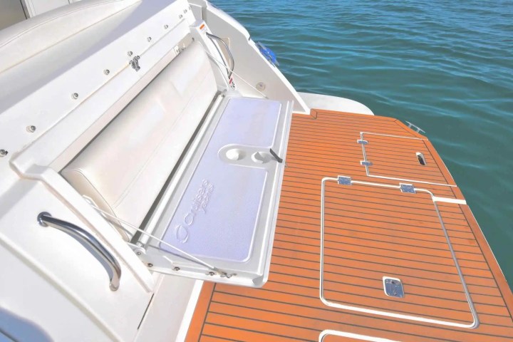 Boat's rear deck with a foldable surface and cup holders, near calm water.