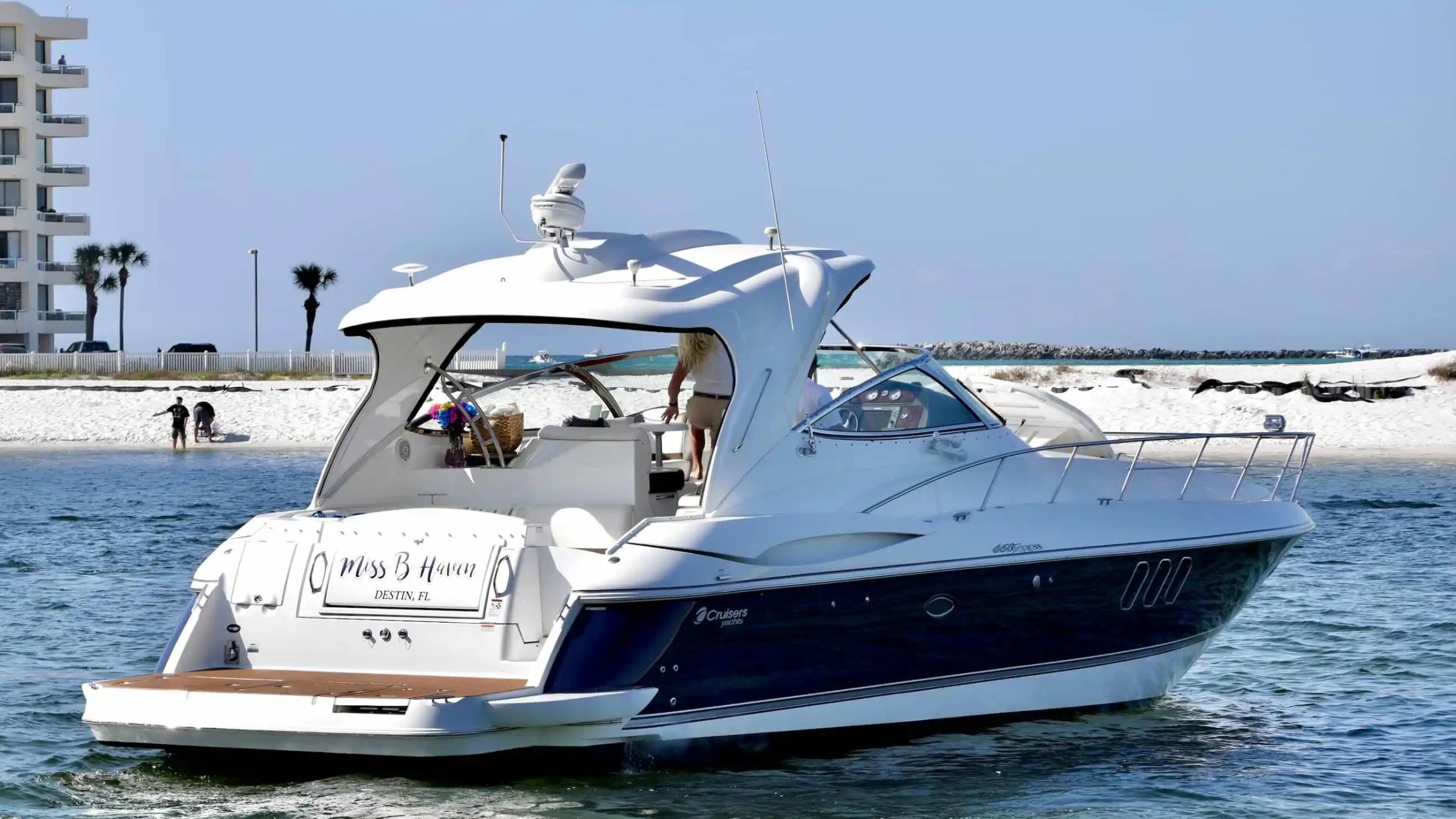 Luxury yacht on water near a sandy beach with people and palm trees in the background.