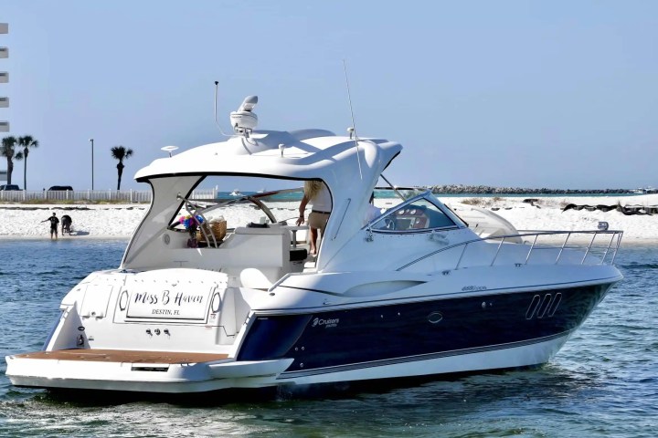 Luxury yacht on water near a sandy beach with people and palm trees in the background.
