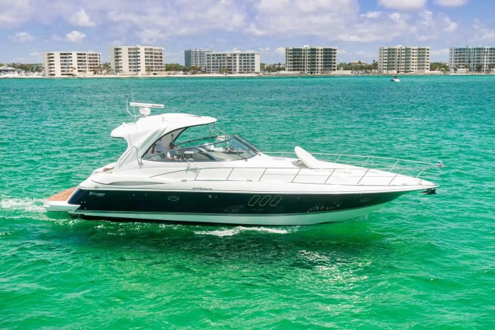Motor yacht cruising on turquoise water near high-rise buildings on a sunny day.