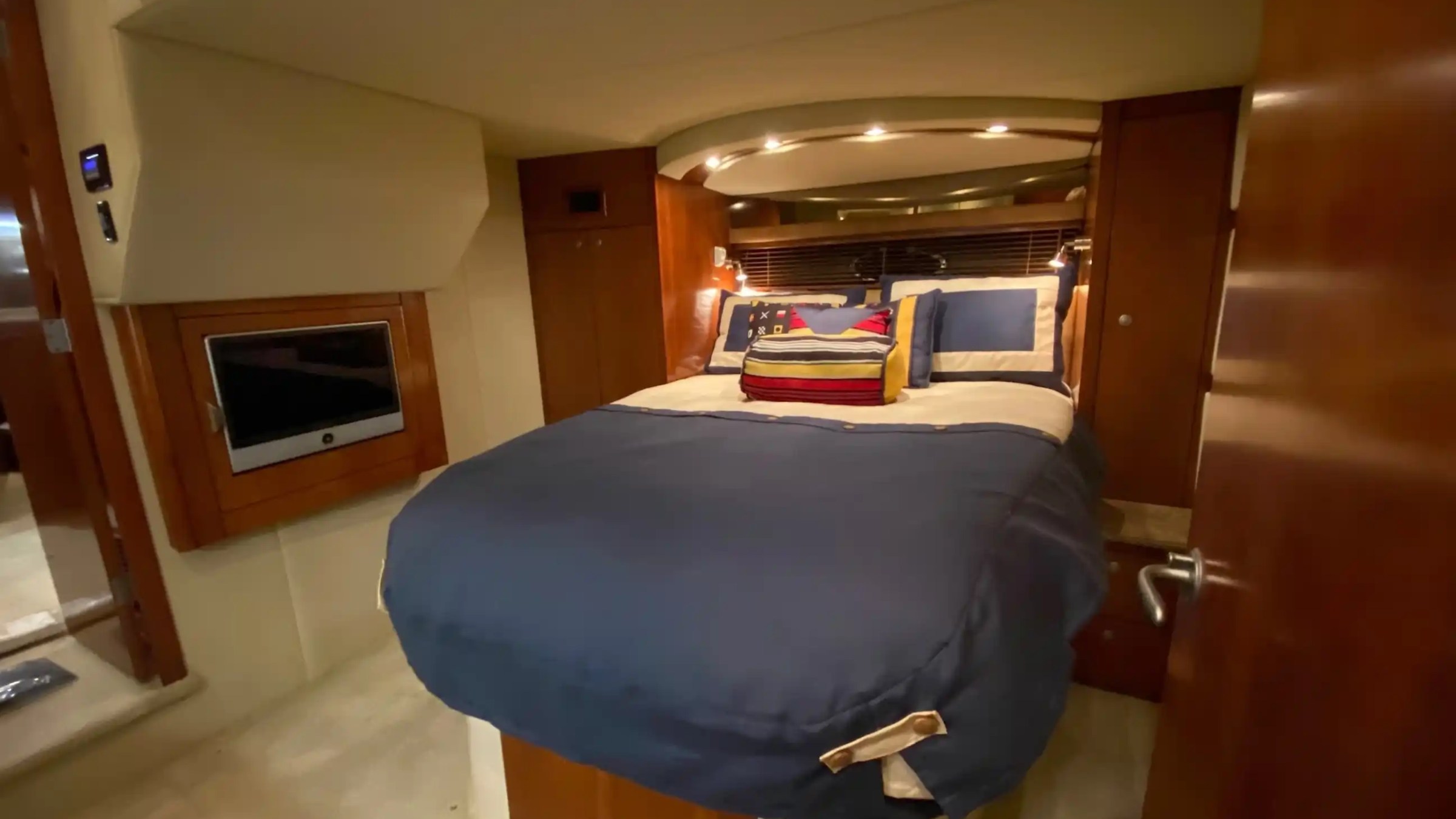 Cozy yacht cabin with a neatly made bed in blue, wood paneling, and a small wall-mounted TV.