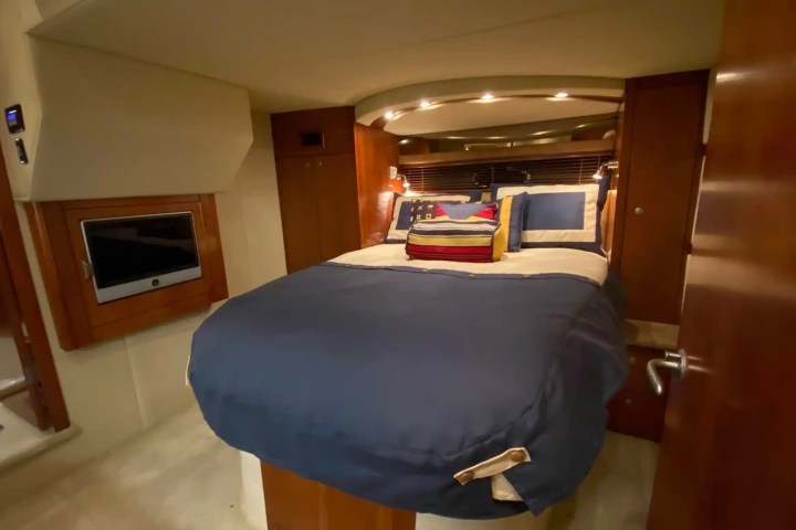 Cozy yacht cabin with a neatly made bed in blue, wood paneling, and a small wall-mounted TV.