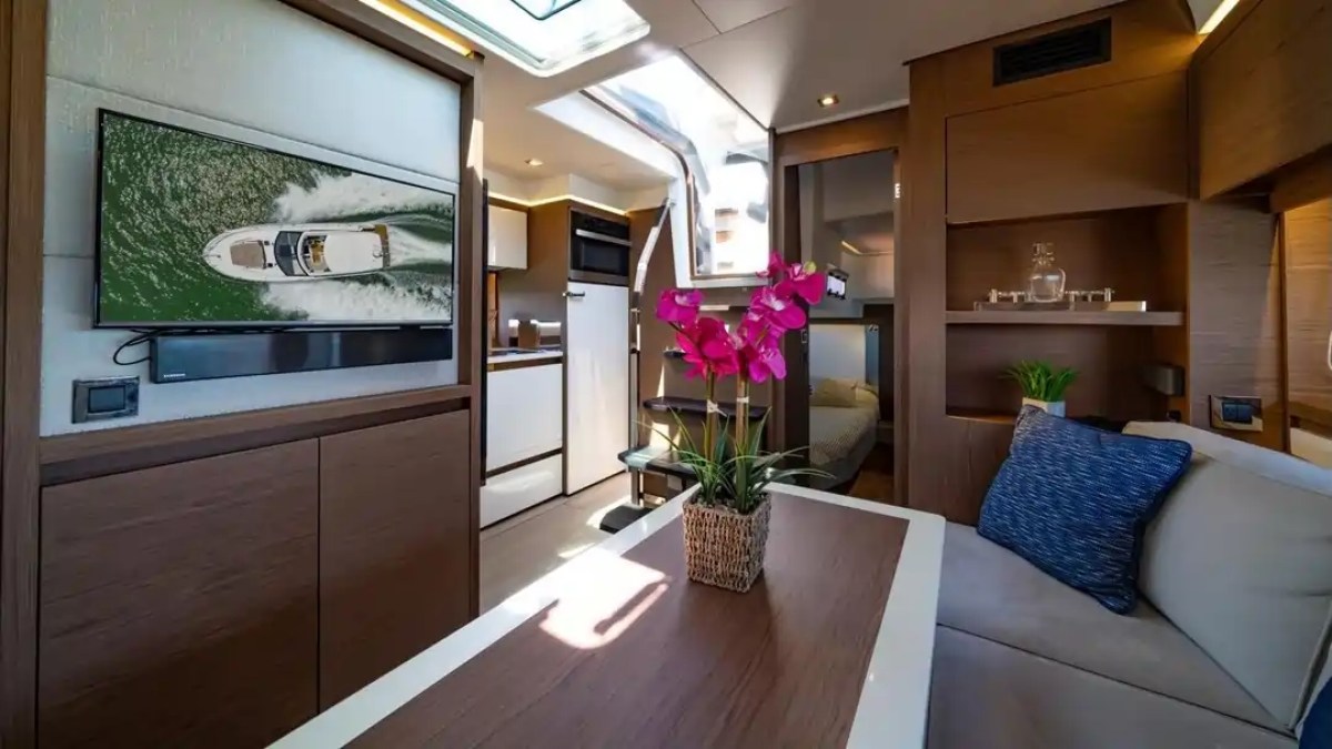 Modern yacht interior with dining table, TV, and pink flowers, featuring wood accents and natural light.