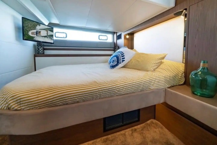 Yacht bedroom with striped bedding, decorative pillow, TV, and a green glass bottle on a wooden surface.
