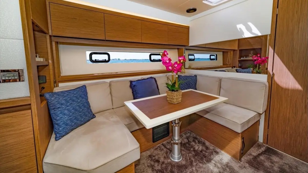 Modern boat interior with beige seating, blue cushions, a table, and pink flowers in a vase.