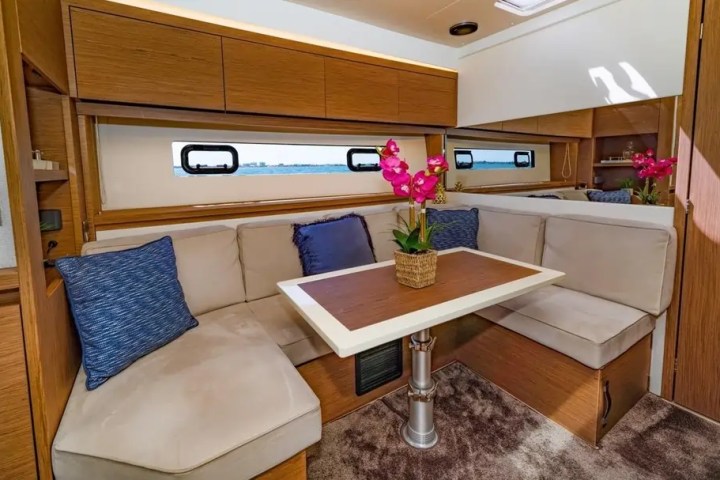 Modern boat interior with beige seating, blue cushions, a table, and pink flowers in a vase.