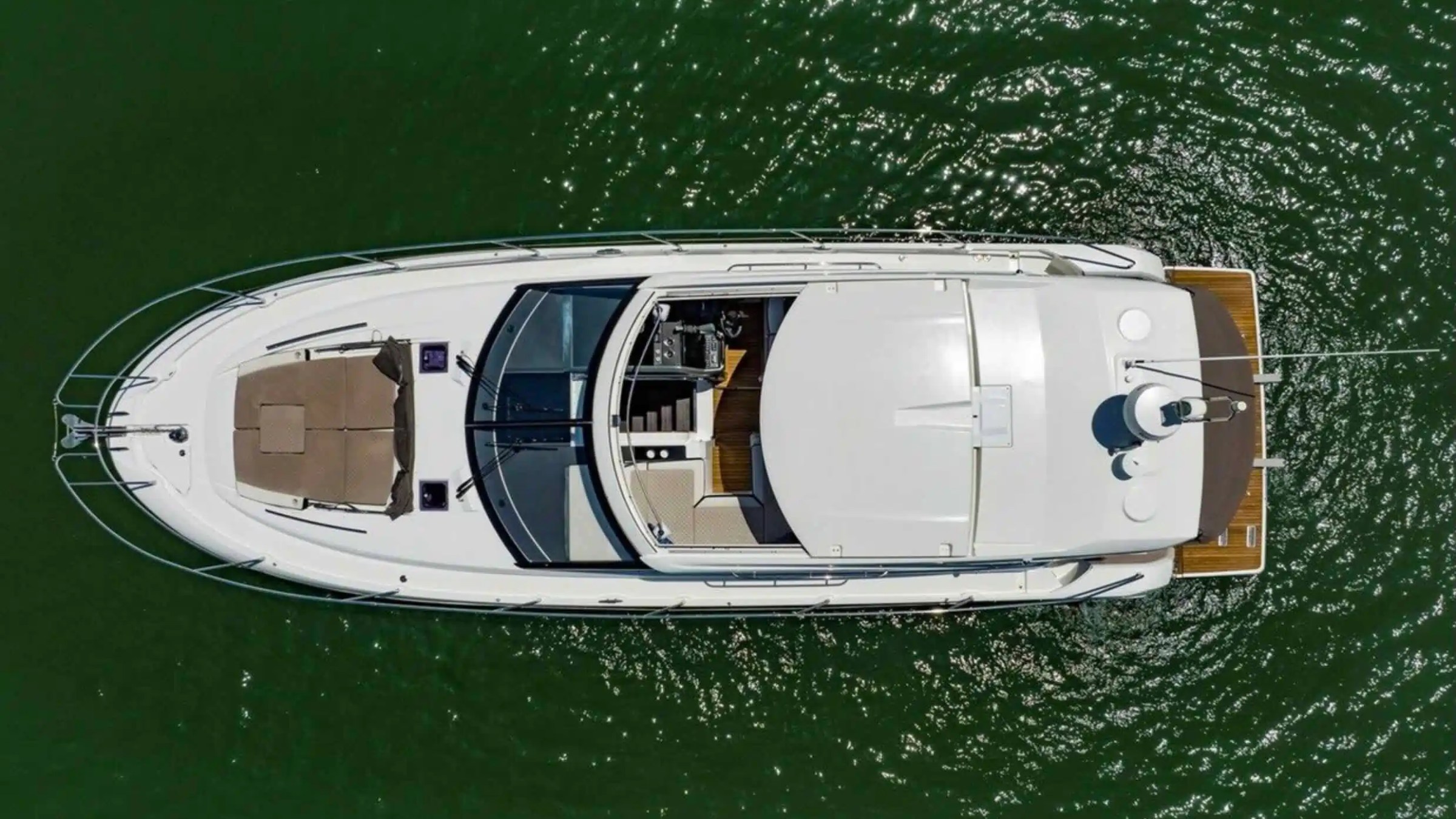 Aerial view of a yacht on green water with visible deck and sunbeds.