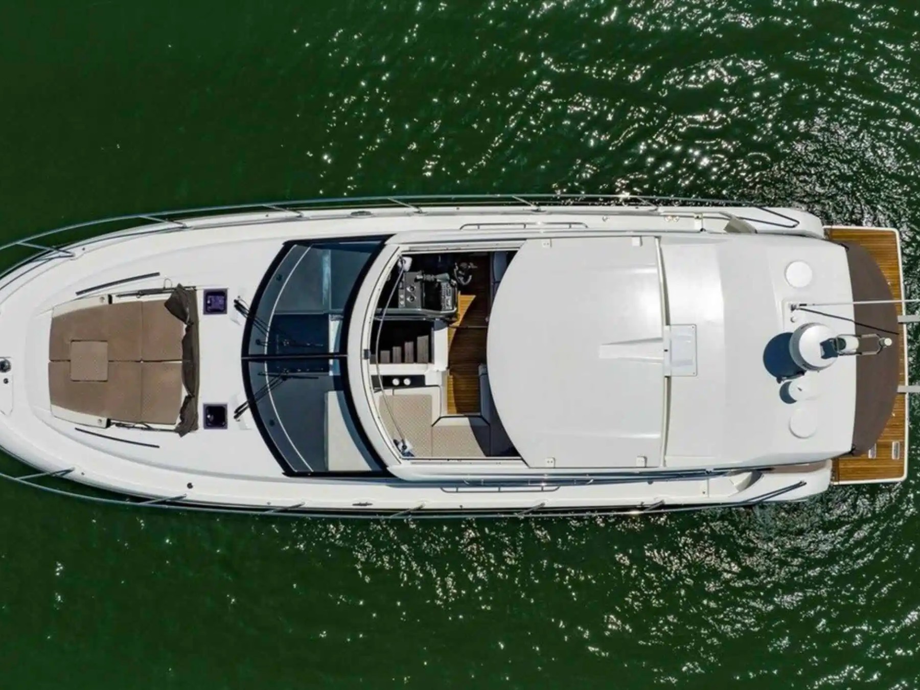 Aerial view of a yacht on green water with visible deck and sunbeds.