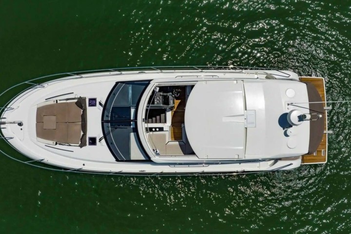 Aerial view of a yacht on green water with visible deck and sunbeds.
