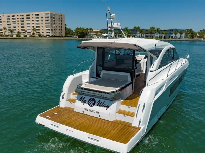 White yacht named 'My Way' in calm water near a row of palm trees and buildings.