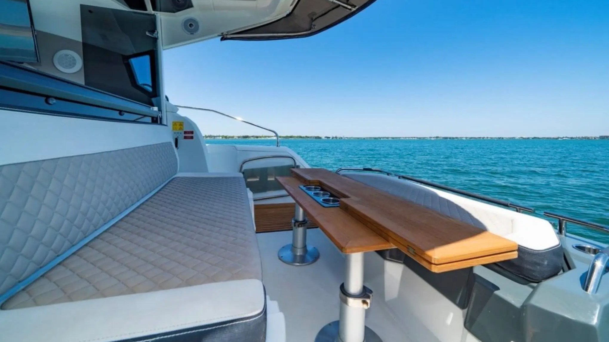 Boat interior with cushioned seating, wooden table, and ocean view.