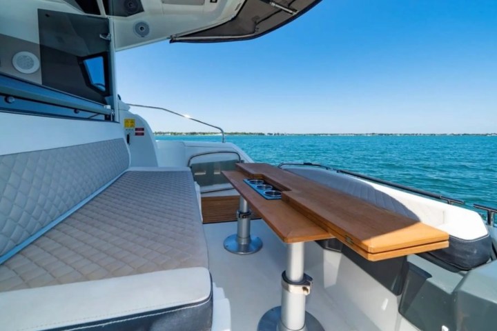 Boat interior with cushioned seating, wooden table, and ocean view.