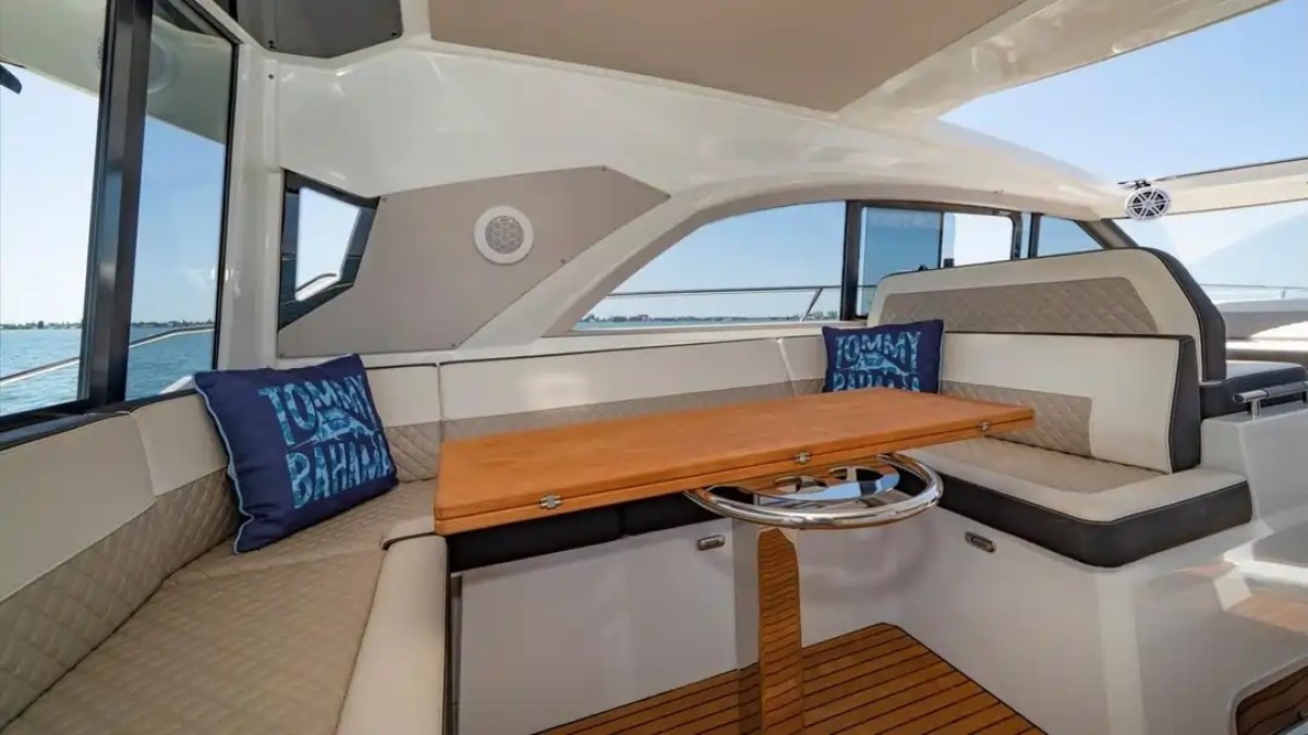 Boat interior with L-shaped seating, wooden table, and Tommy Bahama pillows near windows.