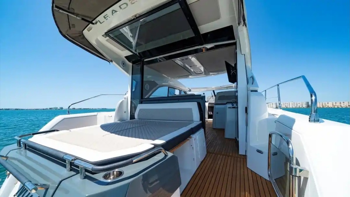 Luxury yacht deck with sunbed, modern interior, and sea view under clear blue sky.