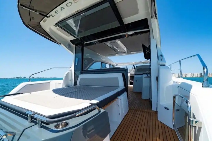 Luxury yacht deck with sunbed, modern interior, and sea view under clear blue sky.