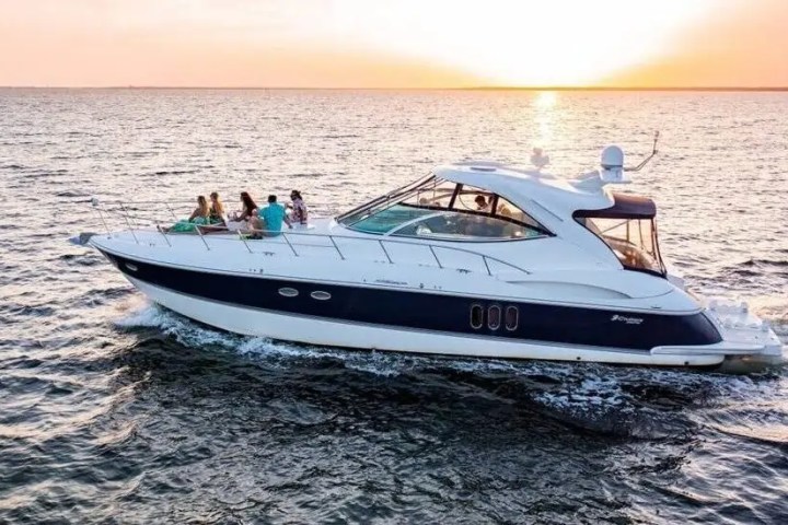 Luxury yacht with people onboard cruises at sunset on open water.