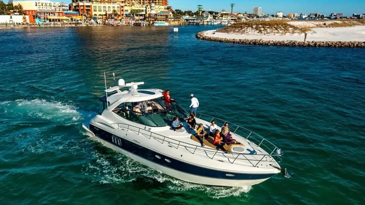 A yacht with people on board cruising in clear water near a coastal city.