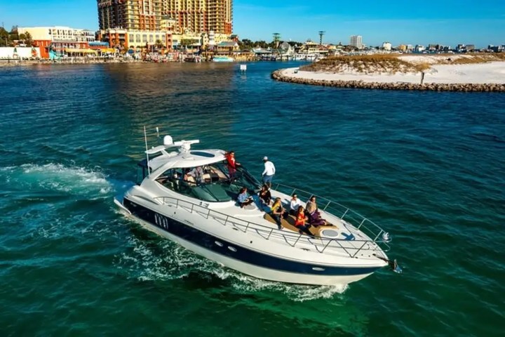 A yacht with people on board cruising in clear water near a coastal city.