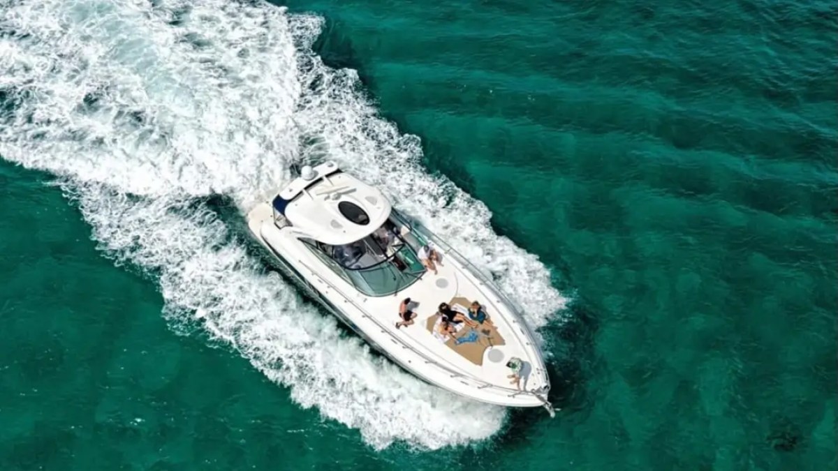 Aerial view of white yacht with people sailing in clear turquoise water.