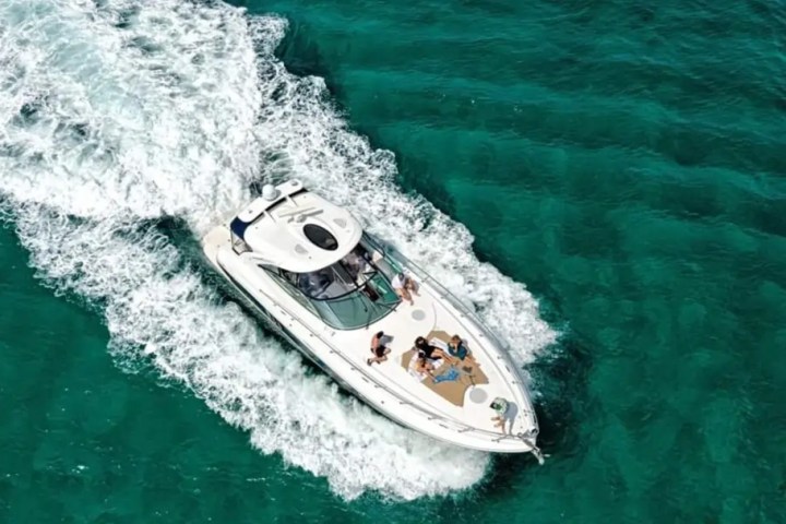 Aerial view of white yacht with people sailing in clear turquoise water.