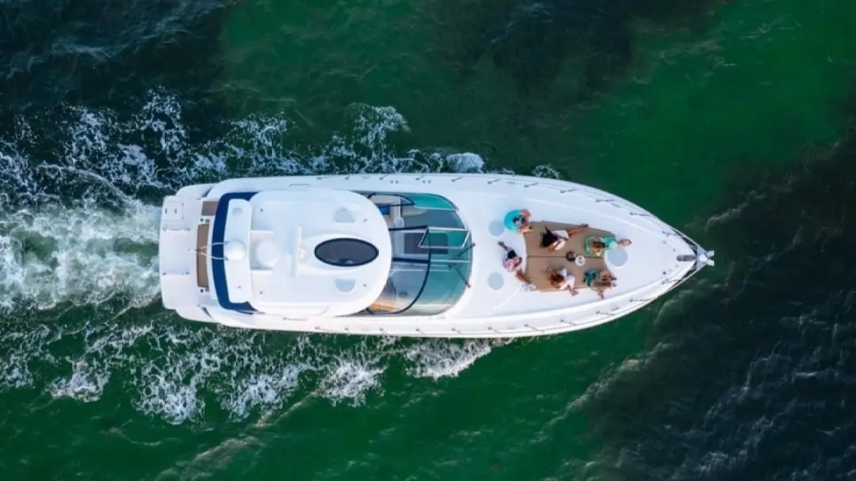 Aerial view of a yacht with people on deck in green water.