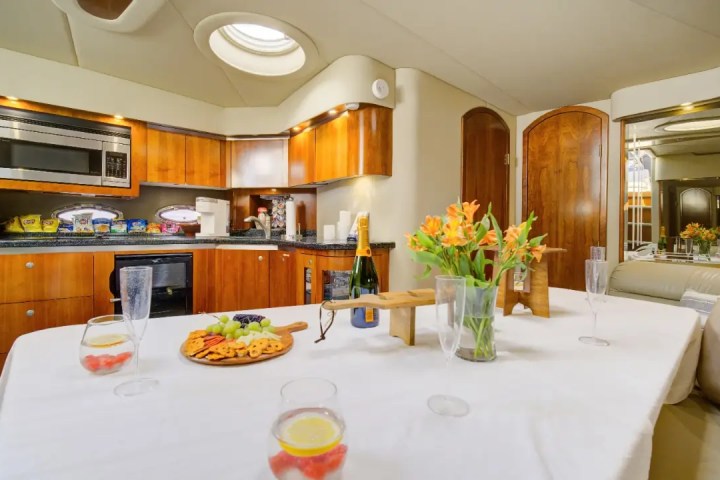 Luxury kitchen with wooden cabinets, table set with flowers, fruit platter, and champagne bottle.