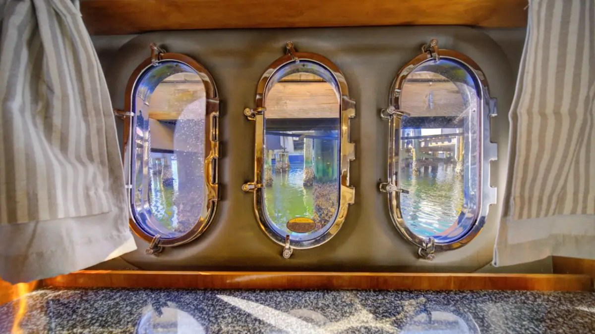 Boat interior with three round windows showing a view of water and dock pilings.