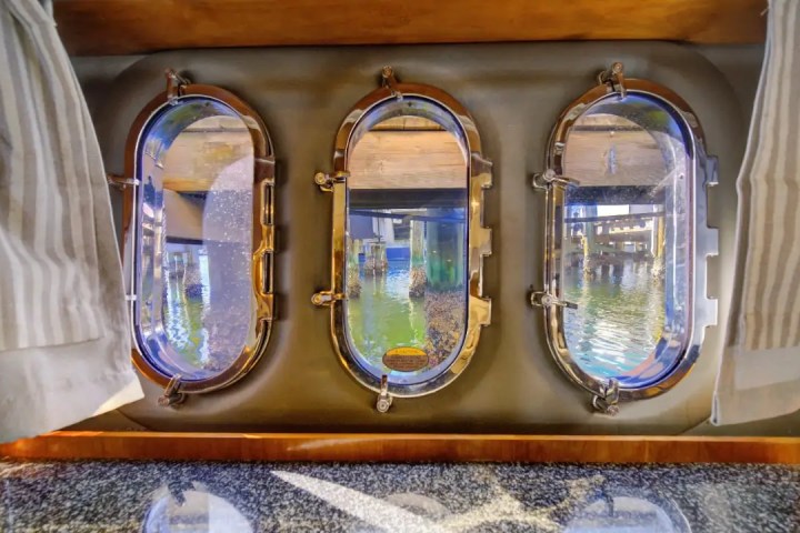 Boat interior with three round windows showing a view of water and dock pilings.